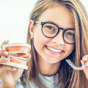Girl holding sample braces in one hand and clear aligner in the other