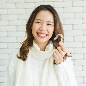 Woman in white sweater holding Invisalign smiling