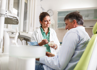 Smiling dentist showing patient model of teeth